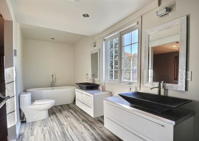 Cette pièce est littéralement une salle de bain de rêve! De style spa, elle est spacieuse, élégante, raffinée et apaisante grâce à ses matériaux naturels : vasques et base de douche en pierre. La céramique à l’apparence de bois ajoute au style spa. Le plancher chauffant jusque sous la douche apporte un confort exceptionnel à la pièce. Le bain autoportant avec sa robinetterie sur pied vient compléter cet endroit de détente parfaite.