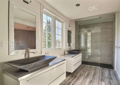 Cette pièce est littéralement une salle de bain de rêve! De style spa, elle est spacieuse, élégante, raffinée et apaisante grâce à ses matériaux naturels : vasques et base de douche en pierre. La céramique à l’apparence de bois ajoute au style spa. Le plancher chauffant jusque sous la douche apporte un confort exceptionnel à la pièce. Le bain autoportant avec sa robinetterie sur pied vient compléter cet endroit de détente parfaite.