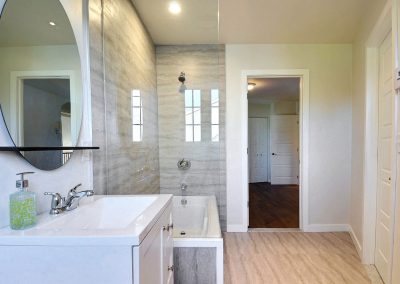 Cette pièce a subi une transformation spectaculaire. L’ensemble des changements ont rendu la pièce beaucoup plus lumineuse, spacieuse et moins étouffante. Le mur au bout du bain a été remplacé par un mur de verre qui permet la circulation de la lumière dans toute la pièce, dégageant du même coup l’espace visuel. La céramique autour du bain est la même que celle du plancher ce qui crée une belle continuité dans la pièce et contribue à agrandir visuellement l’espace. Les plaintes de bois ont été remplacées par des plaintes sobres et blanches. Les meubles modernes et blancs complètent cet ensemble chic et apaisant.