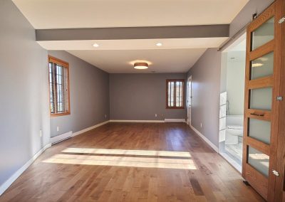 Le tapis a été remplacé par le plancher de bois franc choisi pour l’ensemble de la maison. Ce nouveau plancher donne beaucoup de chaleur à la pièce et augmente la luminosité dans la pièce en reflétant la lumière naturelle qui entre dans la pièce par ses magnifiques fenêtres en bois. Une belle porte à panneaux ferme désormais la garde-robe. La salle de bain quant à elle, est maintenant fermée par une magnifique porte coulissante vitrée et en chêne teint de la même couleur que le plancher. Cette porte, faite sur mesure, est définitivement un élément clé donnant une ambiance « chic industriel » à la pièce.